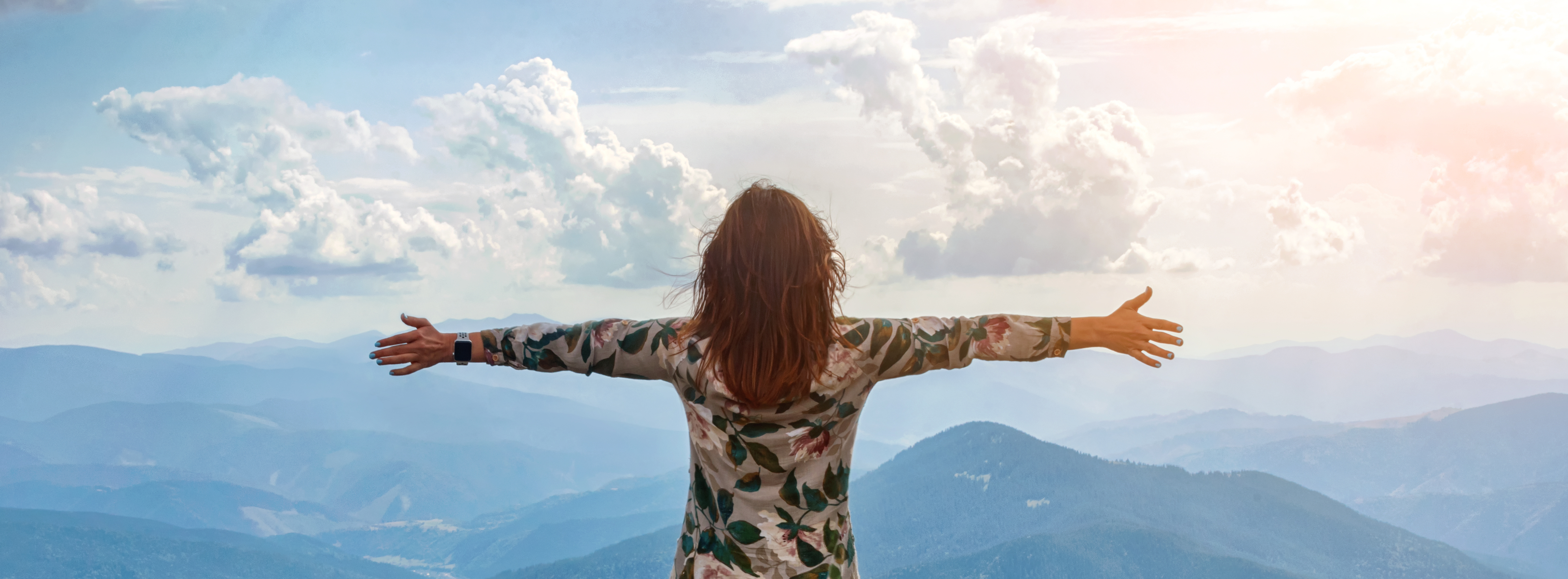 Femme libre les bras ouverts face à un paysage montagneux, symbolisant la libération.